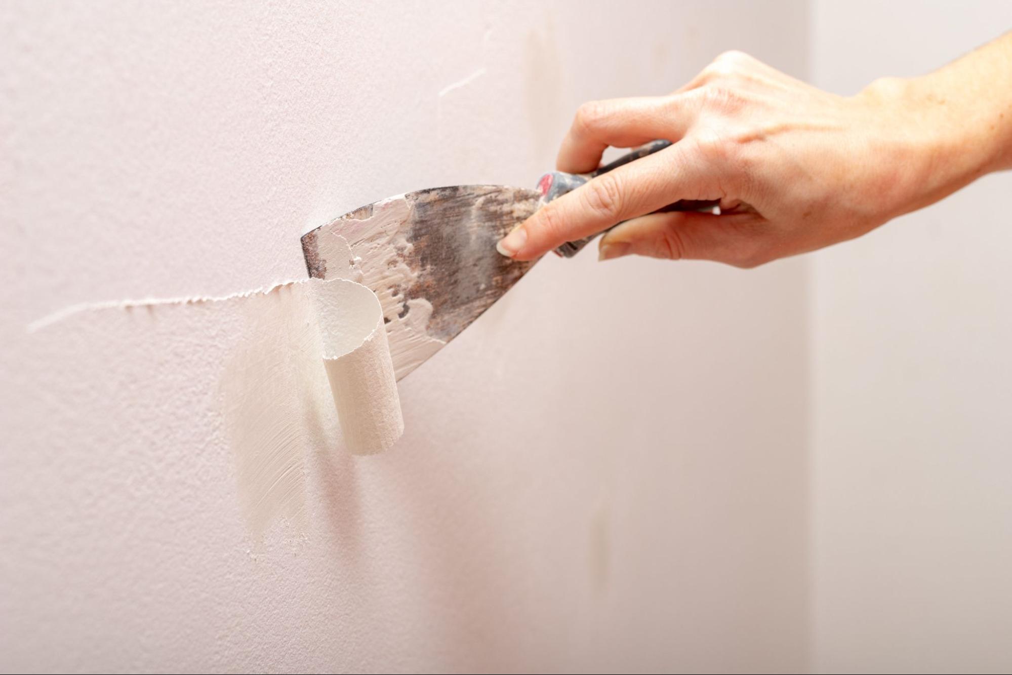 A handywoman scraping old paint from a wall